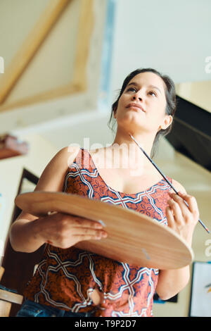 Portrait der hispanischen junge Frau Malerei in Ihrem Haus Studio, Training mit Farbe, Pinsel, Staffelei und Farbe für Hobby. Stockfoto