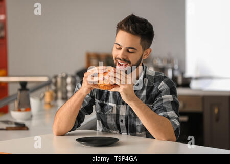 Junger Mann essen leckere Burger zu Hause Stockfoto