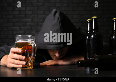 Betrunkene junge Mann mit Bier am Tisch in der Nähe der schwarzen Wand. Alkoholismus Konzept Stockfoto