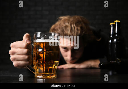 Betrunkene junge Mann mit Bier am Tisch in der Nähe der schwarzen Wand. Alkoholismus Konzept Stockfoto