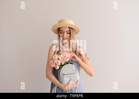 Schöne junge Frau mit Blumenstrauß und Rucksack auf grauem Hintergrund Stockfoto