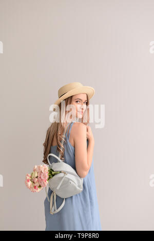 Schöne junge Frau mit Blumenstrauß und Rucksack auf grauem Hintergrund Stockfoto