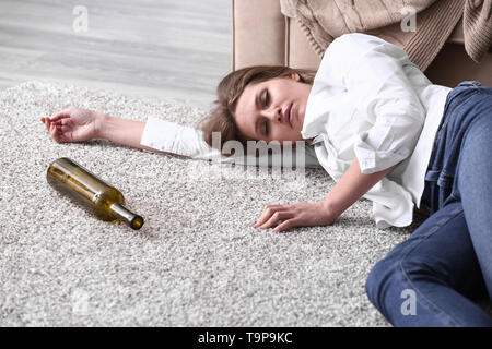 Unbewusste betrunkene Frau mit leeren Flasche liegend auf dem Boden Stockfoto