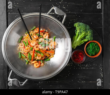 Chinesische Nudeln mit Garnelen und Gemüse im Wok auf hölzernen Tisch Stockfoto