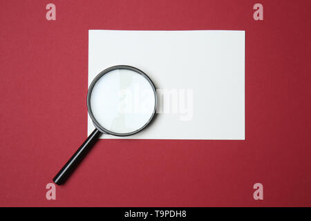 Leeres Blatt Papier mit Lupe auf farbigen Hintergrund Stockfoto