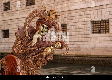 Porträt einer Masculin maskierte Person in einem schönen kreativen Harlekin Kostüm, in den Arkaden des Dogenpalastes, Palazzo Ducale posing Stockfoto