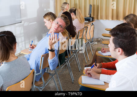 Junge intelligente männliche Kursteilnehmer sprechen mit seinem groupmate während des Unterrichts im Auditorium Stockfoto