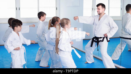 Lächelnde Kinder Karate Tritte mit männlichen Trainer während Karate Klasse Stockfoto