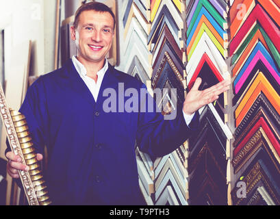 Fröhlicher mann Arbeiter holding Bilderrahmen details zu Counter im Studio Stockfoto