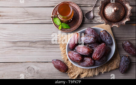 Frische Medjool Datteln in eine Schüssel mit Tee. Ramadan Kareem. Holz- Hintergrund. Ansicht von oben. Kopieren Sie Platz. Stockfoto