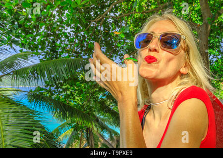 Kaukasische touristische Frau küssen eine niedliche Phelsuma sundbergi namens La Digue Taggecko auf ihre Hand auf den Seychellen. Blonde Frau genießt mit einer Eidechse Stockfoto