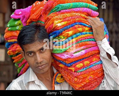 Indische Verkäufer trägt einen Stapel von bunten Stoff auf seine Schulter. Stockfoto