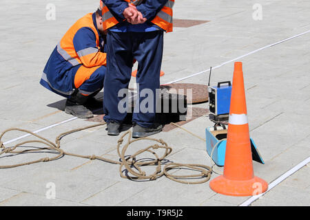 Arbeiter in Uniform stand über dem offenen Abwasserkanal Klappe auf der Straße. Konzept der Reparatur von Abwasser, unterirdischen Versorgungsleitungen, Kabelverlegung, Wasserleitung Unfall Stockfoto