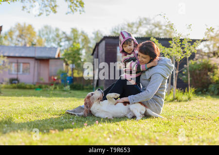 Oma mit Enkelin und Hund Spielen auf der Liegewiese. Sonniger Frühlingstag im Dorf. Stockfoto