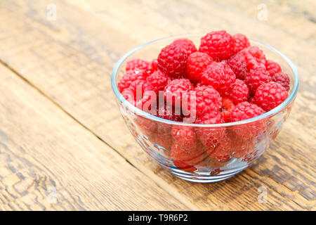 Reife Himbeeren in die Glasschale auf Holzplatten. Frische Beeren im Garten gepflückt. Stockfoto