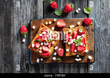 Sandwiches von geröstetem Brot mit Erdnussbutter, in Scheiben geschnittene Erdbeeren und Marshmallows auf einem alten rustikalen Tabelle, Ansicht von oben, flatlay, close-up Stockfoto