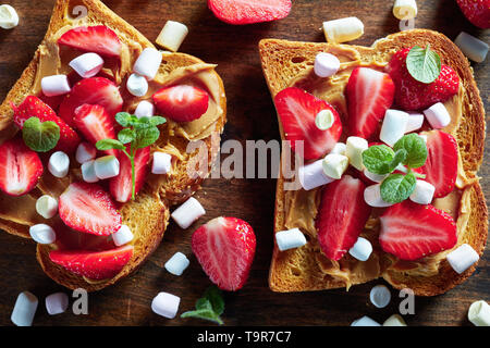 Sandwiches von geröstetem Brot mit Erdnussbutter, in Scheiben geschnittene Erdbeeren und Marshmallows auf einem hölzernen Schneidebrett, Nahaufnahme, Makro Stockfoto