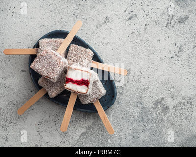 Hausgemachte raw lamington Eis springt auf grauem Hintergrund. Australische süße Nachspeise lamington mit Chia und Himbeeren Marmelade, Schokolade und Kakao. Veganes essen Rezept und Idee. Kopieren Sie Platz. Ansicht von oben Stockfoto