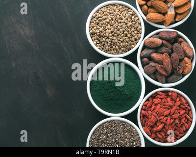 Oben Ansicht von SUPERFOODS wie Chia Samen, Spirulina, Goji Beeren, rohen Kakaobohne, Hanf samen getrocknet, Mandel auf schwarzer Holztisch. Kopieren Sie Platz. Ansicht von oben oder flach-lay Stockfoto