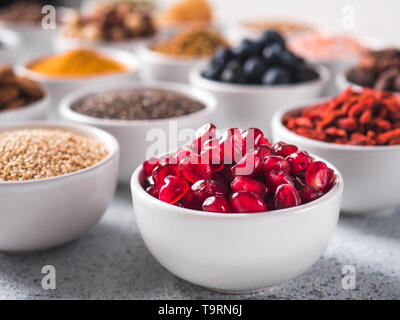 Granatapfel oder Korn der Granat in kleinen weißen Schale und andere superfoods für den Hintergrund. Selektive konzentrieren. Verschiedene superfoods Zutaten. Konzept und Grafik für superfood und entgiftende Lebensmittel Stockfoto