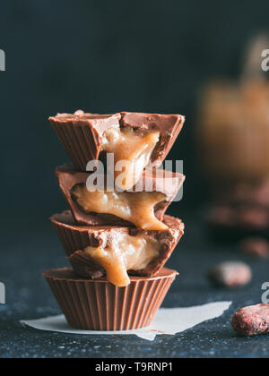 Stapel von vegane Schokolade Tassen mit Karamell auf dunklen Tisch. Hausgemachte vegetarische Chocolate Caramel Cups mit rohem Kakao Schokolade. Ideen und Rezepte für gesunde süße Nachspeise. Kopieren Sie Platz für Text. Vertikale Stockfoto