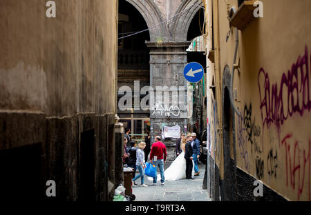 Ein frisch verheiratetes Paar Spaziergang vorbei am Ende der schmalen Gasse in Neapel, Italien. Um sie herum sind Touristen, Einheimischen und der Verkehr auf der Straße. Stockfoto