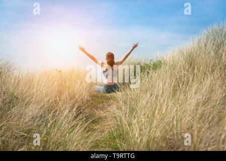 Sportliche Frau in Lotus Position mit den Armen in den Himmel Meditation erhöht sitzen. BCK ANZEIGEN. Stockfoto