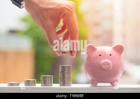 Sparschwein mit Stapel von Münzen, männliche Hand Geld sparen Konzept Stockfoto