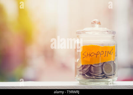 Geld sparen für Shopping Haushalt, Münzen in Glasflasche mit unscharfen Hintergrund Platz für Text Stockfoto