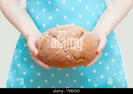 Kaukasische Frau in Schürze holding Roggenbrot Brot in den Händen. Close-up. Stockfoto