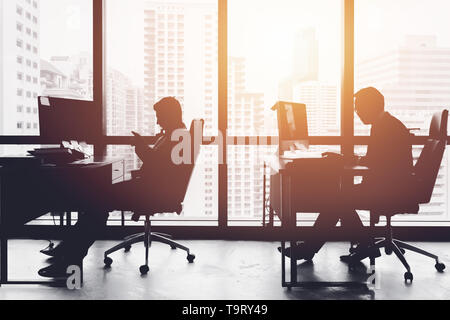 Silhouette business Mann im Büro am Schreibtisch windows Seite arbeiten mit städtischen Stadtblick Stockfoto