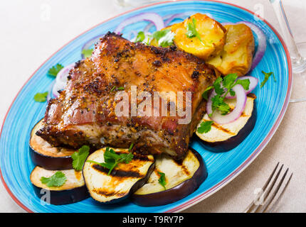 Gegrillte Schweinerippchen Rack garniert auf weiße Platte mit gebackenen Kartoffeln und Auberginen und Frische rote Zwiebel Stockfoto