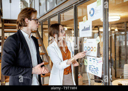 Geschäftsleute in einer Diskussion, die während der Arbeit mit Diagrammen und Zeichnungen auf der Wand im Büro Stockfoto