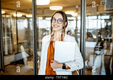 Portrait einer jungen und cherful Business stehende Frau mit Laptop im Büro Stockfoto