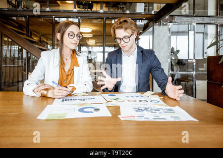 Der Mann und die Frau Arbeiten mit Dokumenten, während sitzen zusammen am Tisch im Büro oder Coworking Space Stockfoto
