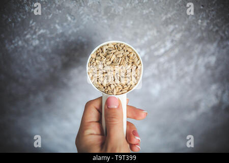 Natürliche Sonnenblumenkerne ohne Schale in den weißen Messbecher von oben auf der grauen und weißen Hintergrund. Stockfoto