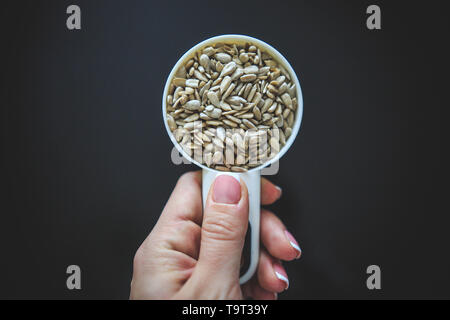 Natürliche Sonnenblumenkerne ohne Schale in den weißen Messbecher von oben auf der Rückseite Hintergrund genommen. Stockfoto