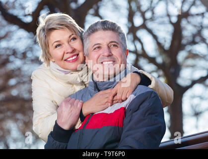 Älterer Mann und Frau umarmen einander sitzen auf einer Parkbank Stockfoto