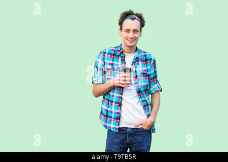 Einen Kaffee Pause. junge Hipster Mann im weißen T-Shirt und kariertem Hemd ständigen Holding Pappbecher mit Kaffee am Morgen mit Hand in der Tasche. Innen- Stockfoto