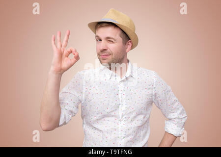 Fröhlicher junger Mann in hat, ok Zeichen Stockfoto