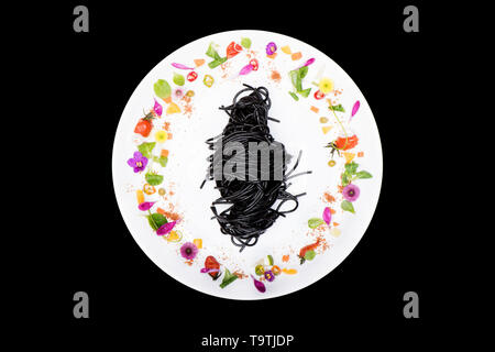 Schwarz squid Spaghetti in der Platte mit Blumenschmuck auf schwarzem Hintergrund Stockfoto