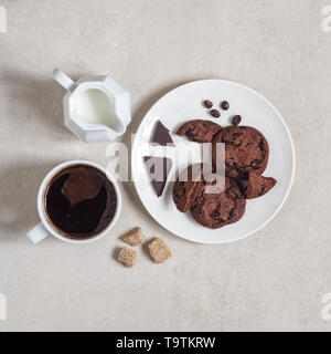 Haferflocken Cookies mit Kakao und Schokolade auf einem weissen Teller, eine Tasse Kaffee und ein Milchkännchen Stockfoto