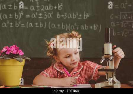 Kleines Mädchen mit Mikroskop in der Schule Labor. Schülerin arbeiten mit Laborausstattung auf Chemie oder Biologie Klasse, vintage Filter Stockfoto