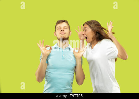 Die schöne junge Paar Brustbild auf Green Studio Hintergrund isoliert. Mann versucht, mit geschlossenen Augen ruhig zu halten, während Frau schreien ist. Mimik, menschliche Emotionen Konzept. Stockfoto