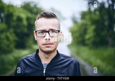 Porträt eines jungen Mannes mit Brillen in Regen. Selektiver Fokus auf Regentropfen. Stockfoto
