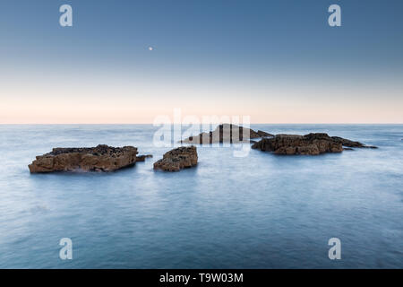 Lange Belichtung Marine vor der britischen Küste mit Felsen und der Mond am Himmel über Stockfoto