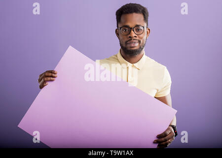 Bild von jungen afrikanischen amerikanischen Mann mit lila Blank Board an der Kamera auf lila Hintergrund suchen, kopieren. Stattliche schwere Kerl mit leeren pl Stockfoto
