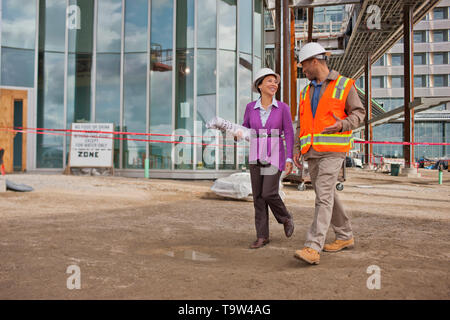 Junge Ingenieurin Holding die Baupläne und in einem freundlichen Gespräch mit dem Vorarbeiter auf einer Baustelle. Stockfoto