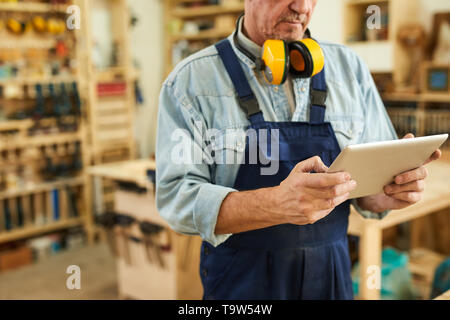 Den mittleren Abschnitt Portrait von älteren Tischler mit Tablette während in der Tischlerei arbeiten, kopieren Raum Stockfoto