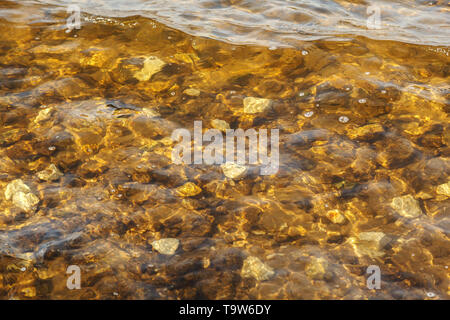 Fluss Wellen in der Nähe der Ufer mit felsigen Boden. Transparente sauberes Wasser Wellen. Zusammenfassung Hintergrund Textur von einige glatte Steine und Sand in einem Fluss Stockfoto